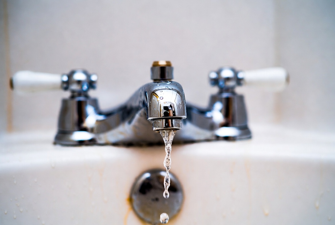 Close-up of a dripping chrome two-handle bathtub faucet with water dripping from the spout